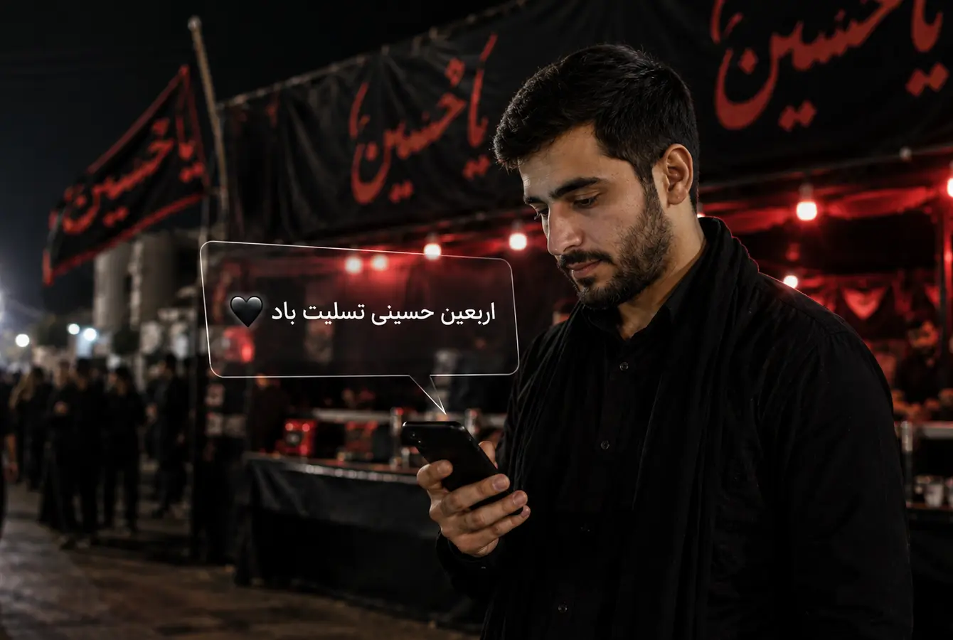 مرد جوانی در موکب اربعین در حال خواندن پیامک تسلیت اربعین حسینی با نورپردازی قرمز و پرچمهای «یا حسین»